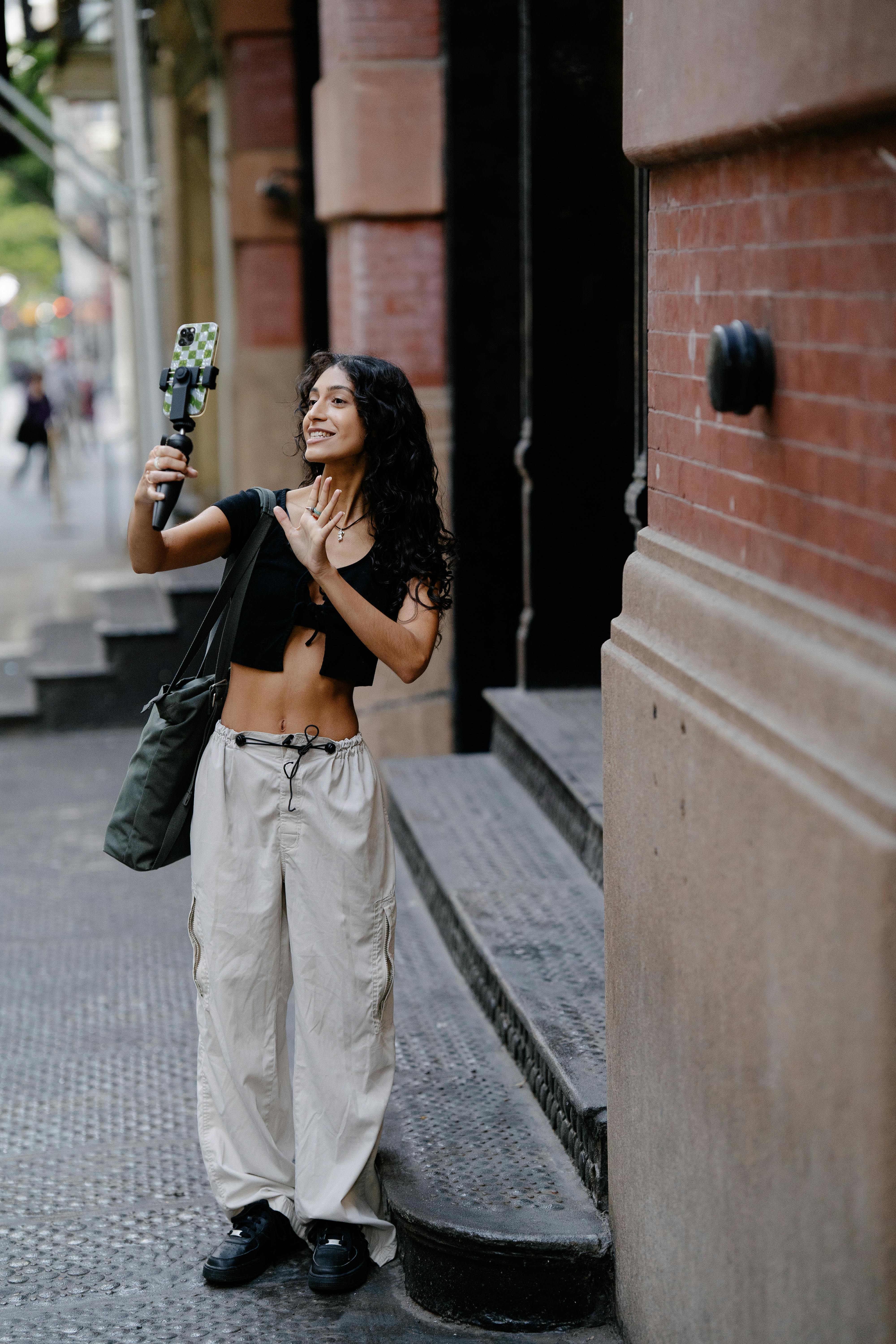 Young woman filming herself with a smartphone on a city street, embracing urban lifestyle.
