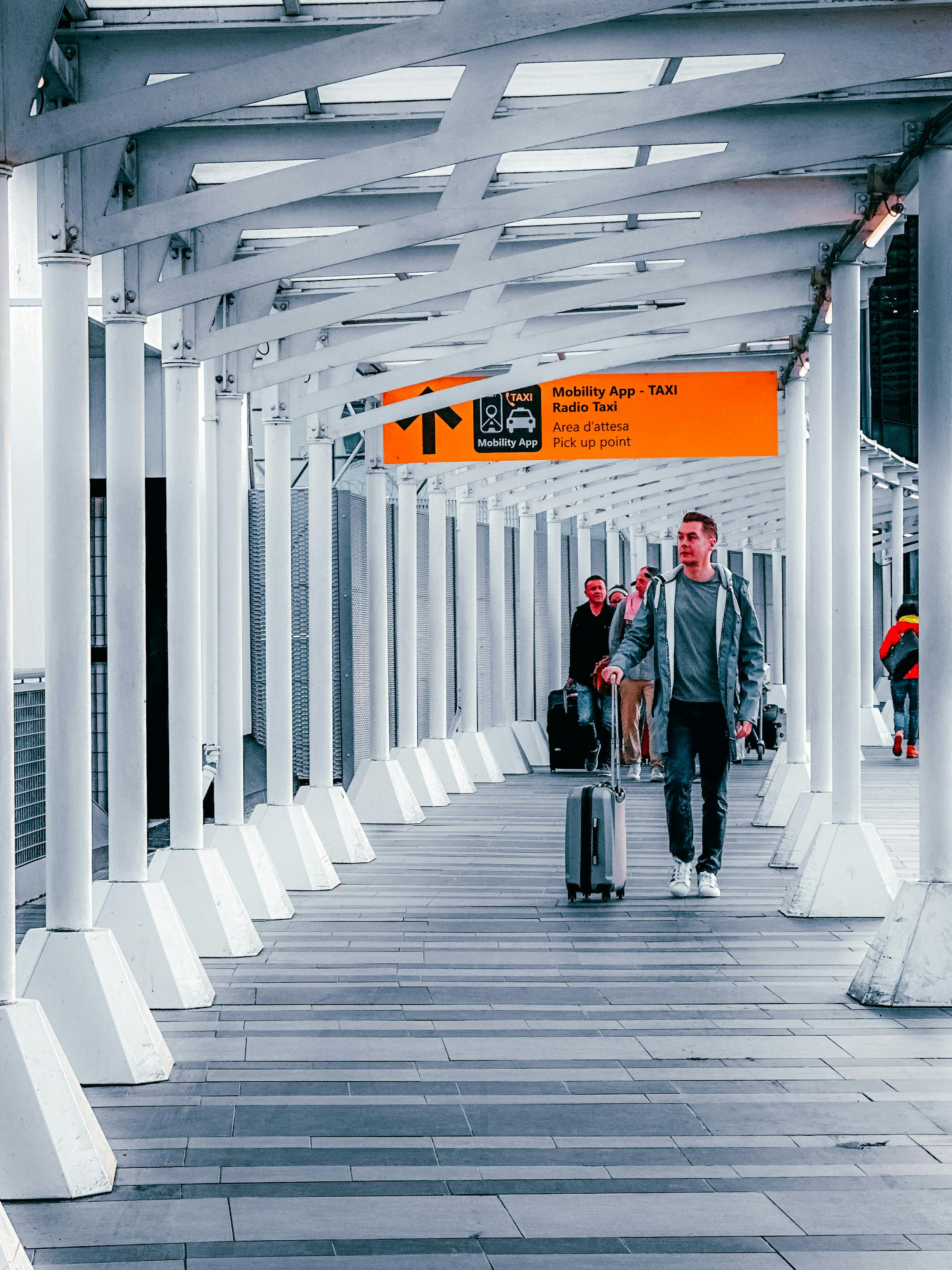 Travelers walking through a modern airport walkway with luggage, heading towards a taxi pickup point.