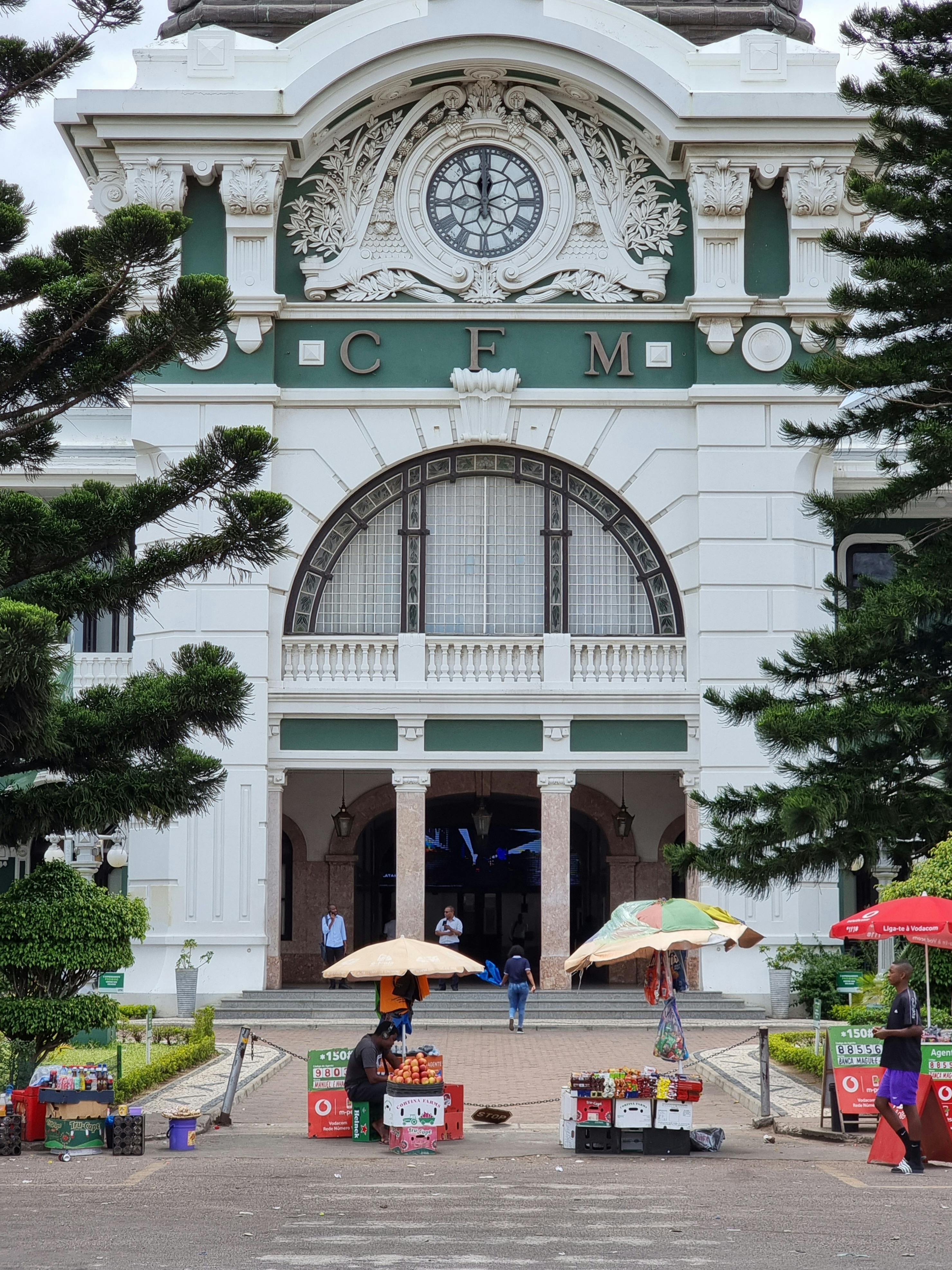 Front view of the Maputo Central Train Station, a historic landmark with vendors outside.
